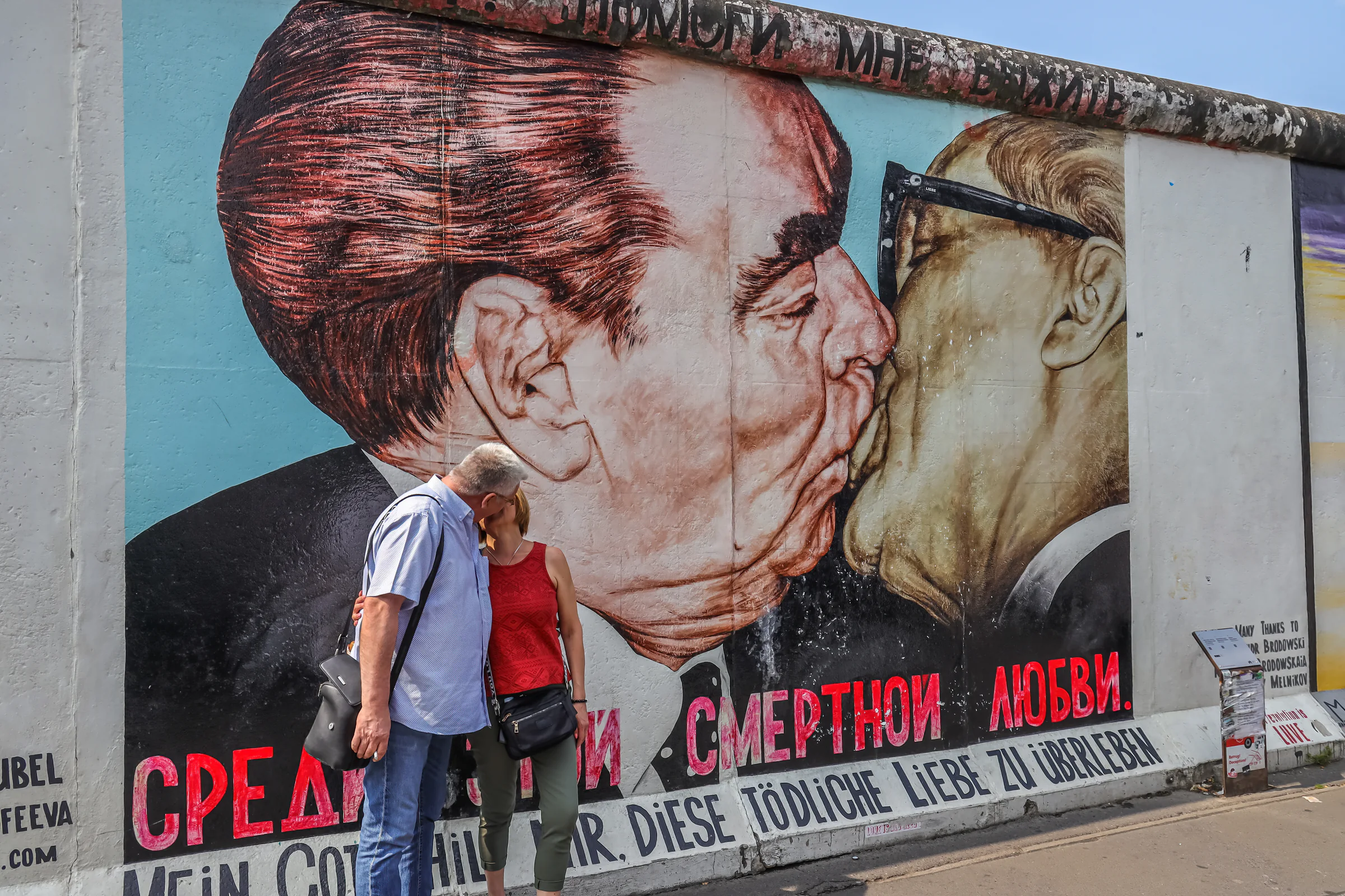 Visitors walking past a large mural on the Berlin Wall