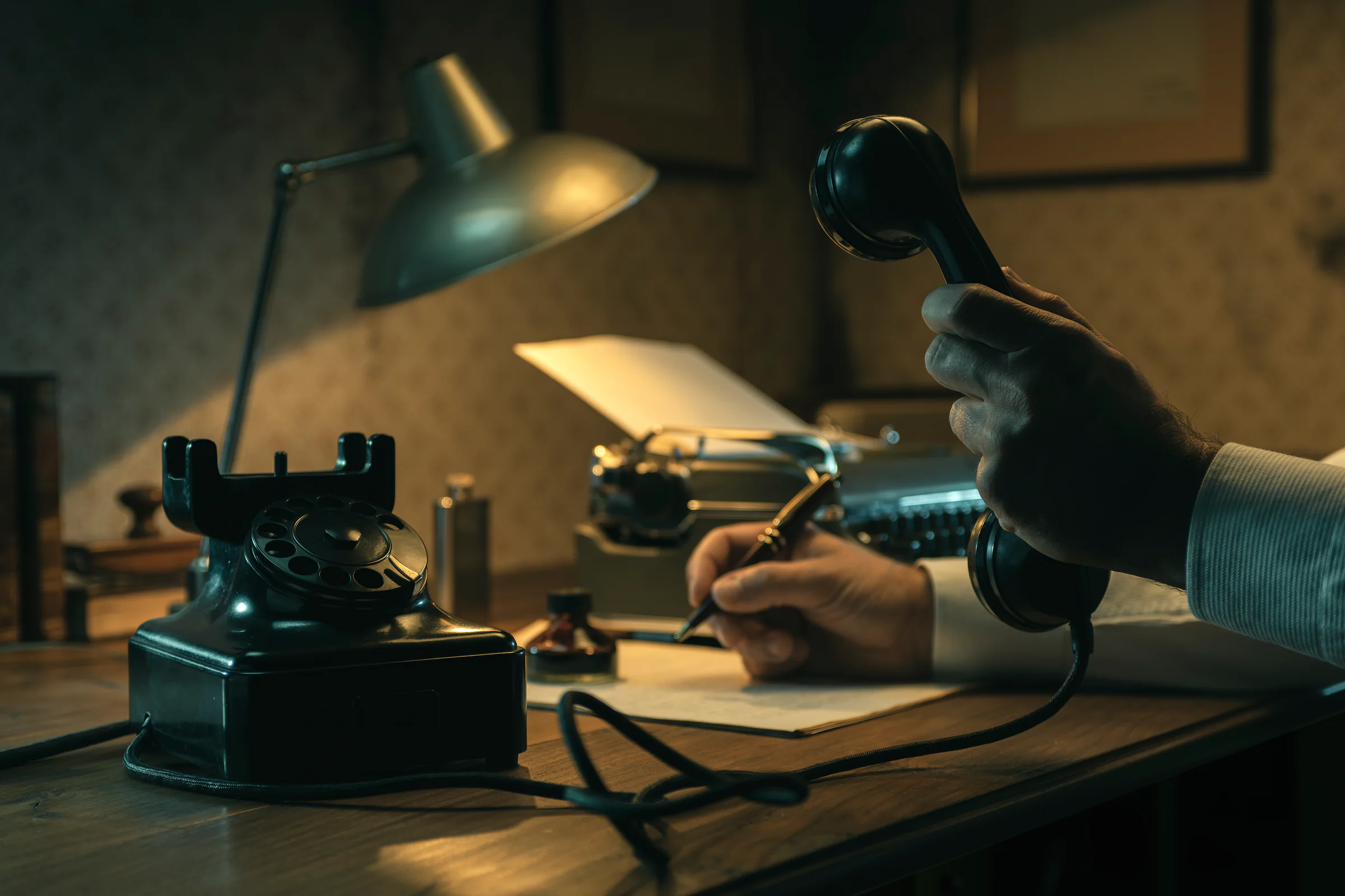Journalist working at a desk beside a telephone in a noir setting